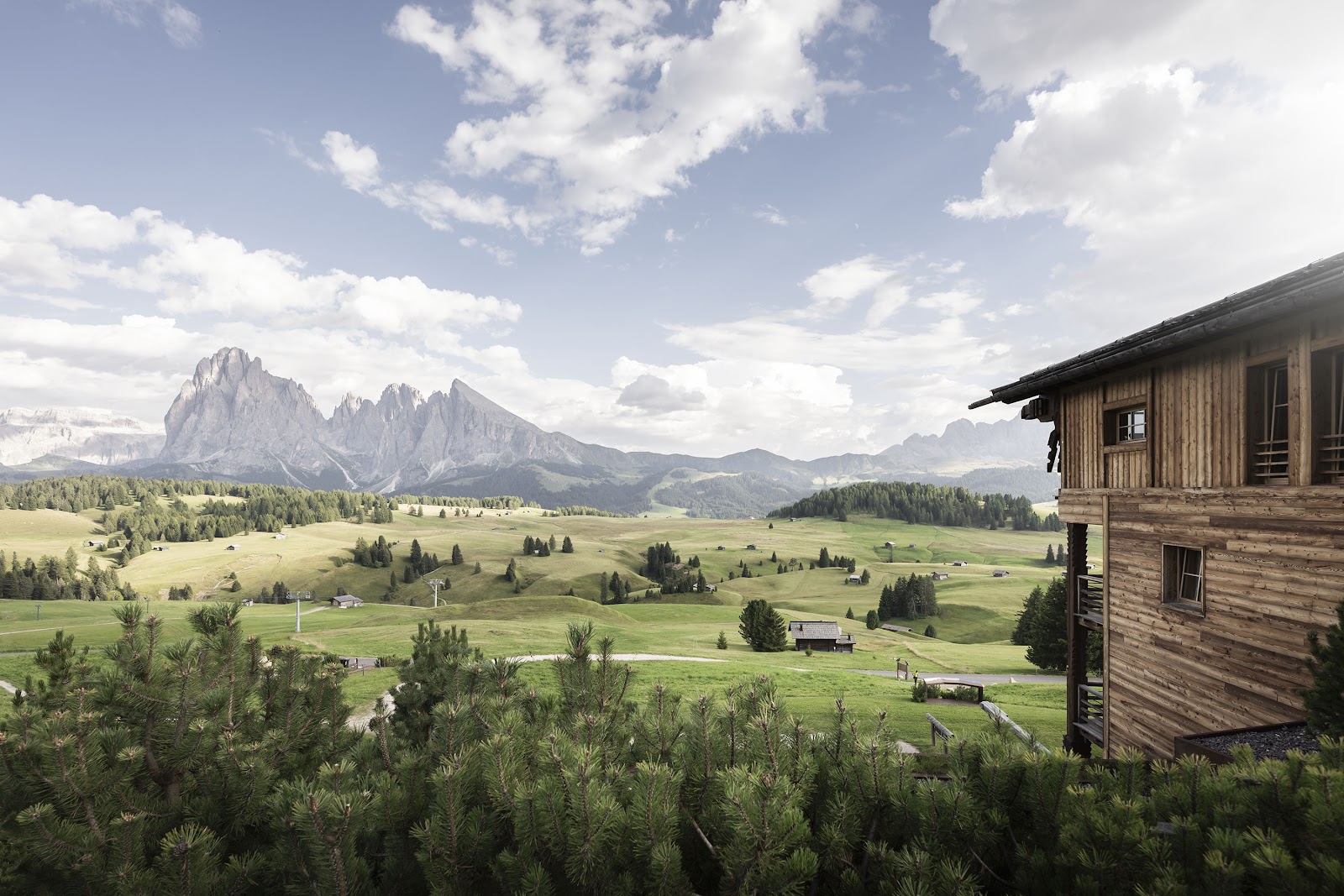 Timber chalets and snow with Dolomite peaks at ADLER Lodge Alpe, Alpe di Siusi